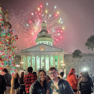 Photo of a couple in front of the South Carolina statehouse with fireworks overhead.
