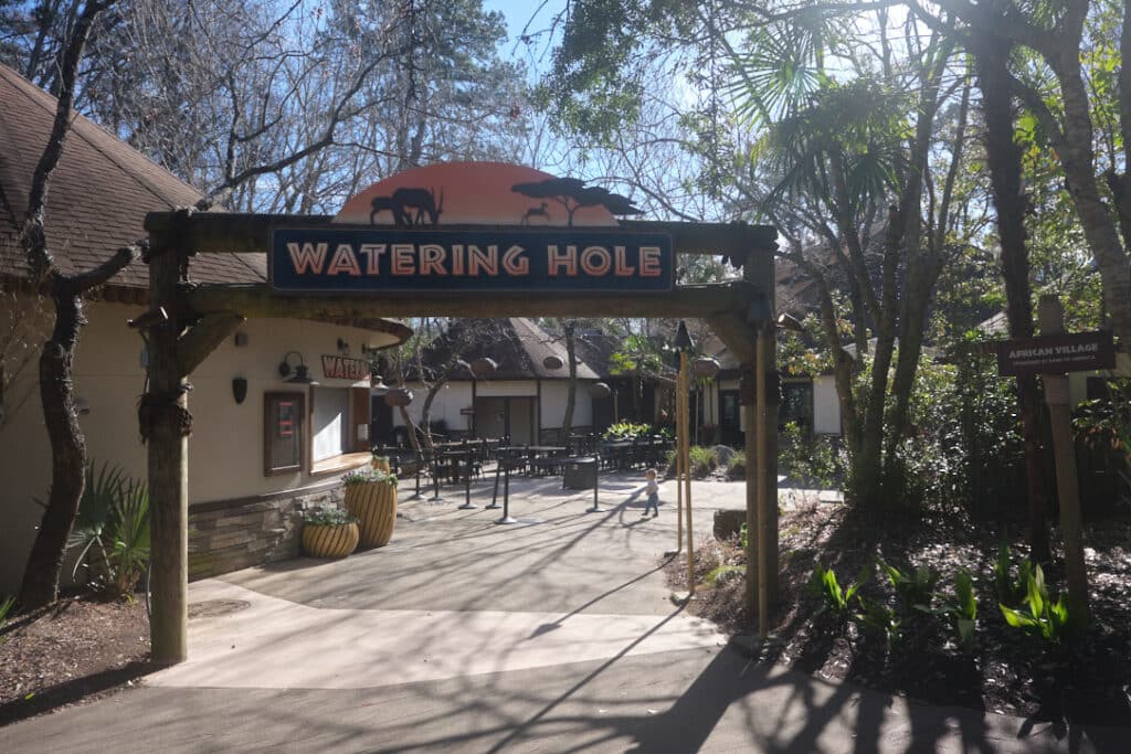 Photo of a sign that says watering hole with tables in the background at the Riverbanks Zoo and Garden.