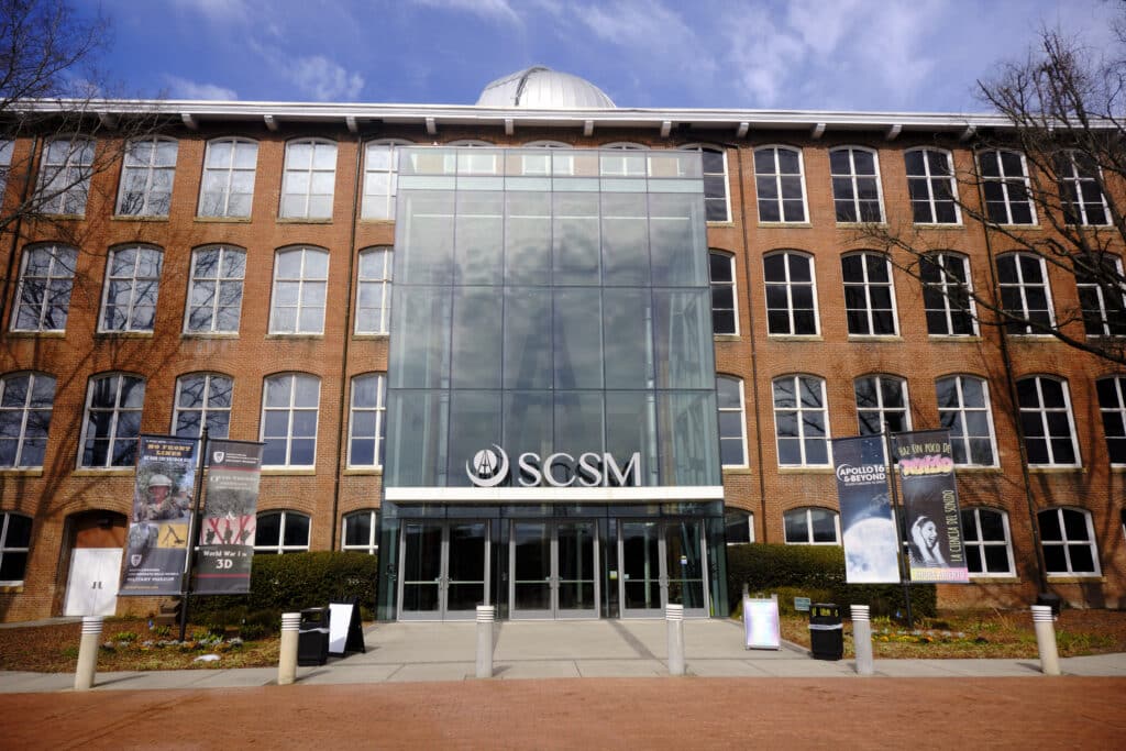 Photo of a large brick building with large windows with the letters SCSM for South Carolina State Museum over the doors.
