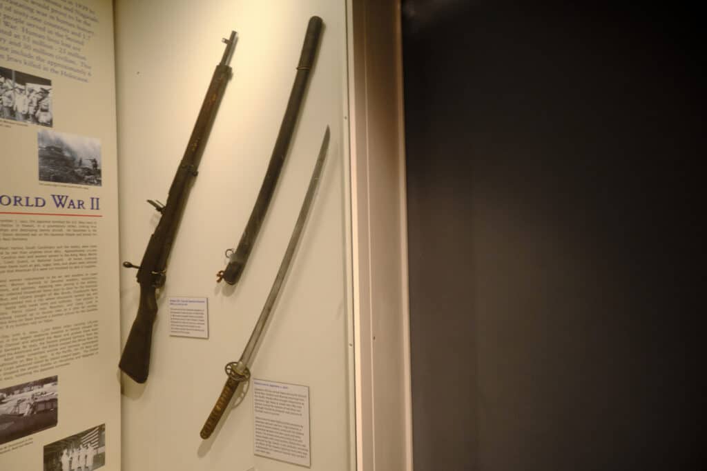 Photo of a rifle next to a sheath and sword mounted on a wall.
