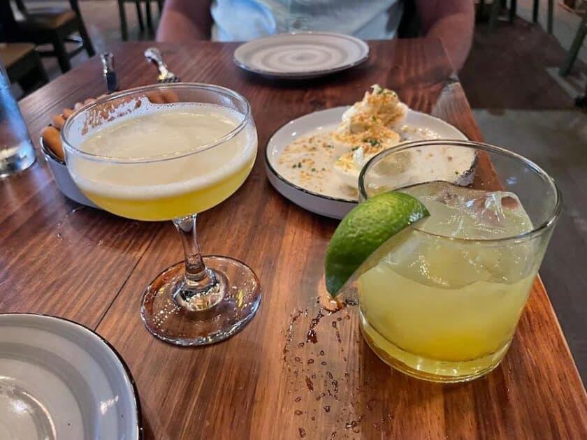 Photo of two Prohibition cocktails on a table with some food behind them.