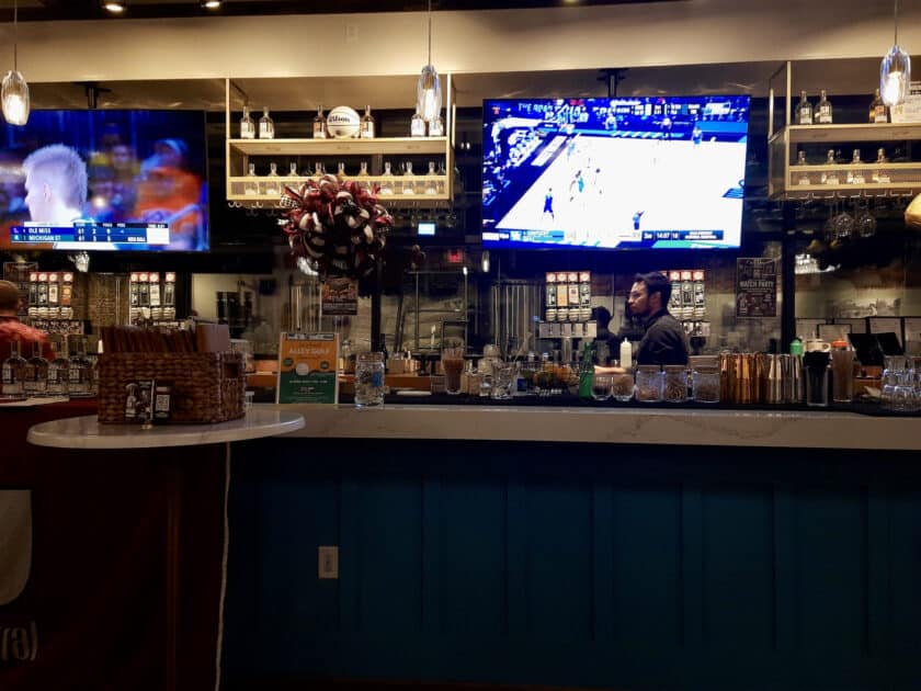 A bar with TV and bartender behind it at Steel Hands Vista Distilling and Brewing.