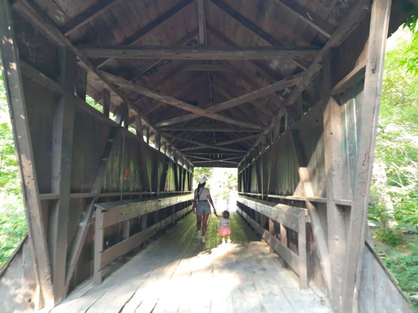 Woman and child holding hands crossing the Pisgah Covered Bridge.