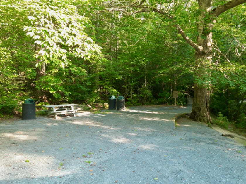 A picnic table and some trash cans by a gravel parking lot at the Pisgah Covered Bridge.