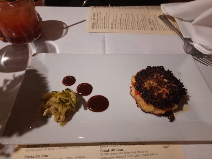 A crab cake with a bit of cucumber relish on a plate at Saluda's Restaurant.