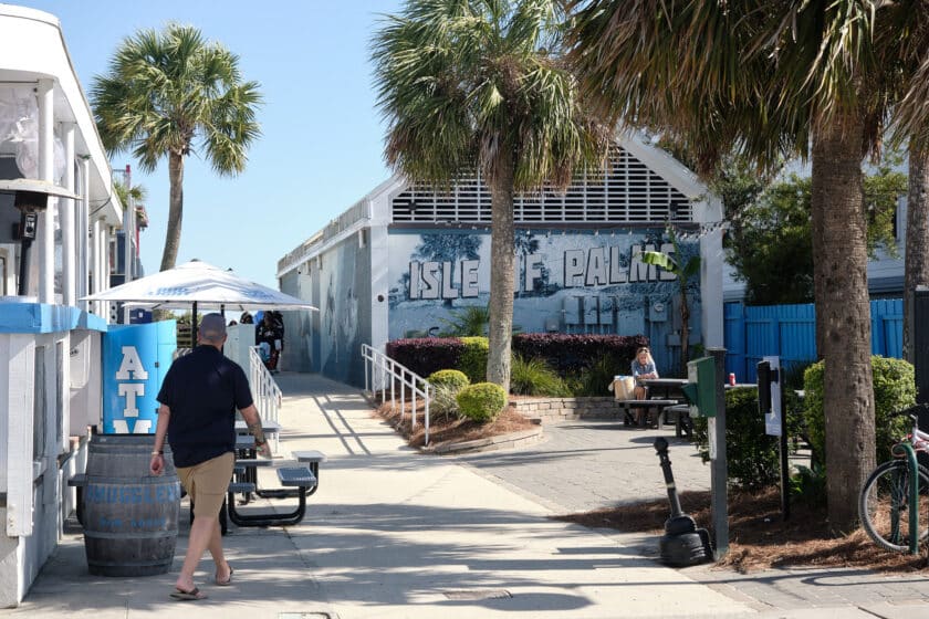 Man walking towards an alleyway out to the beach with a mural that says Isle of Palms in the background.