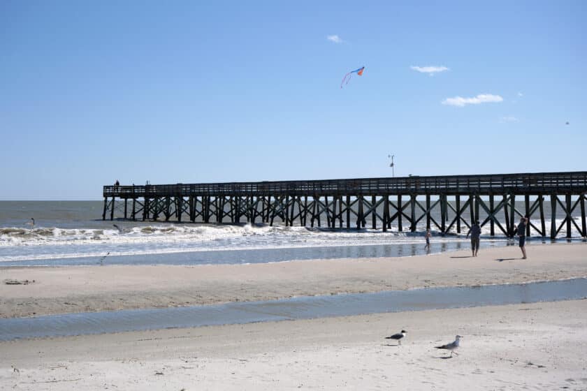 Isle of Palms pier with birds and people on the beach and a kite flying overhead.